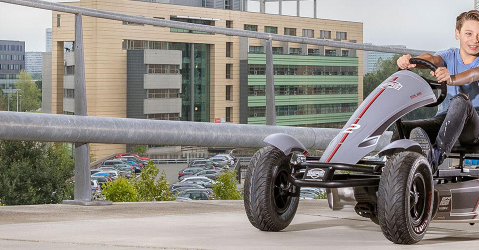 Boy riding a BERG XL Race pedal go-kart on an elevated parking lot in the city, banner