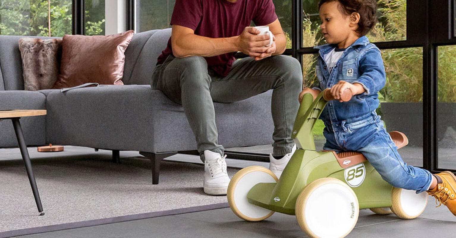 Banner with child on a green BERG GO2 ride-on car in a modern living room